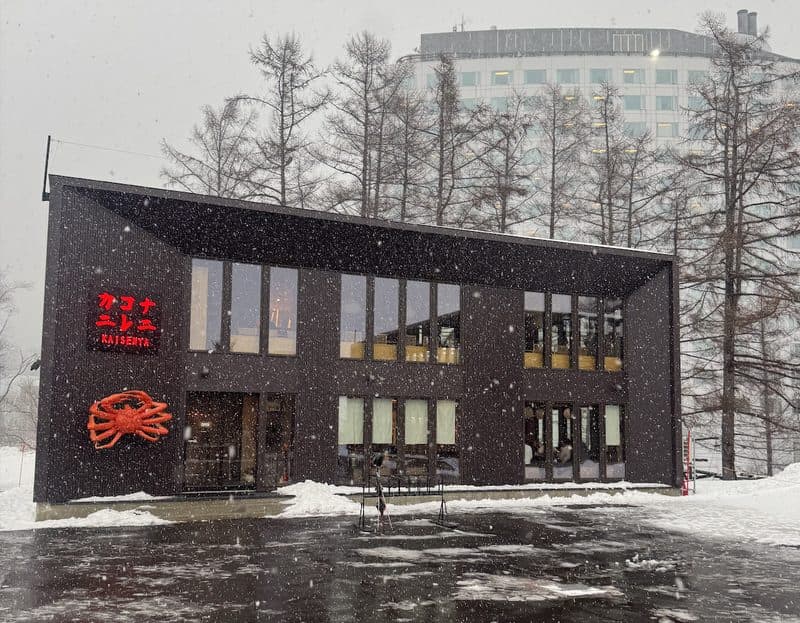 Nani Kore Kani's dark timber exterior and crab sign in falling snow